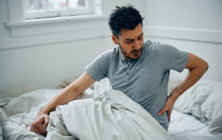 Man sitting on the edge of his bed holding his lower back, experiencing back pain after a car accident