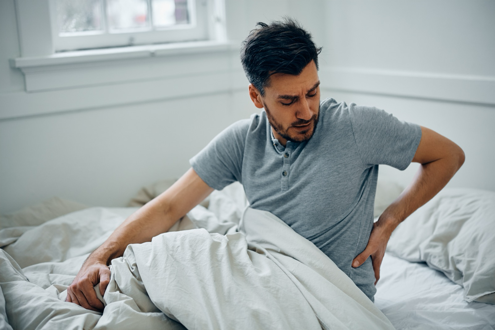 Man sitting on the edge of his bed holding his lower back, experiencing back pain after a car accident