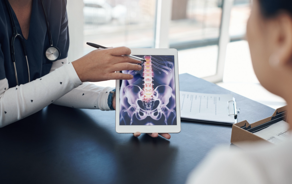 Doctor showing a patient a spine scan on a tablet while explaining MRI vs. X-ray results after a car accident